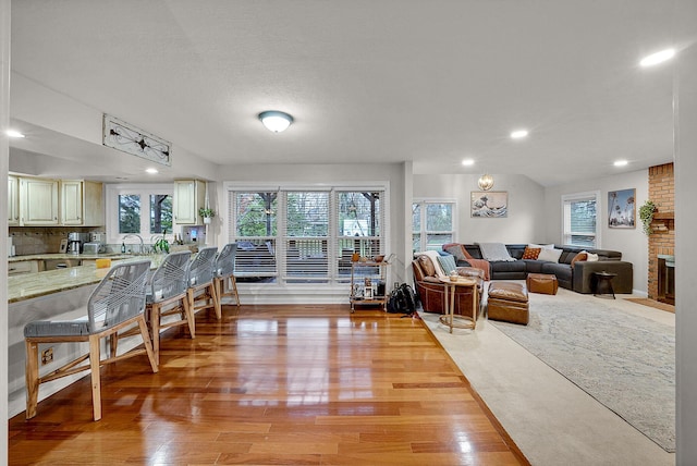 living room featuring lofted ceiling, light wood-type flooring, and a brick fireplace