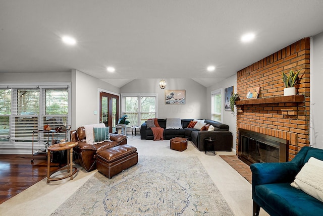 living room featuring wood-type flooring, a brick fireplace, and lofted ceiling