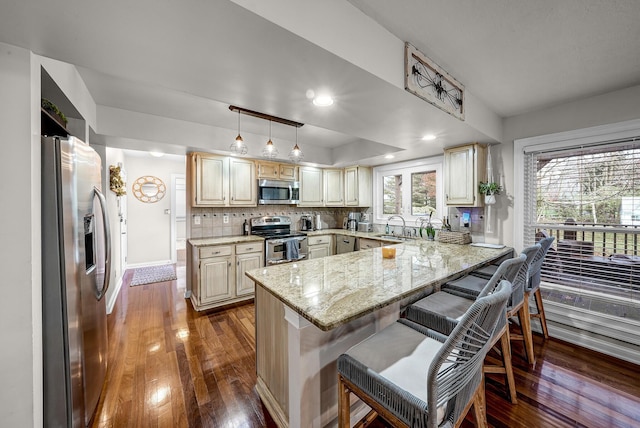 kitchen featuring dark wood-type flooring, hanging light fixtures, appliances with stainless steel finishes, a kitchen bar, and kitchen peninsula