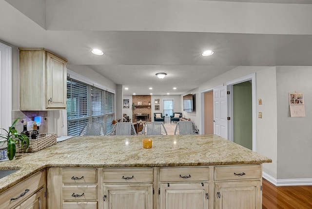 kitchen with light brown cabinets, light hardwood / wood-style flooring, light stone countertops, a fireplace, and kitchen peninsula