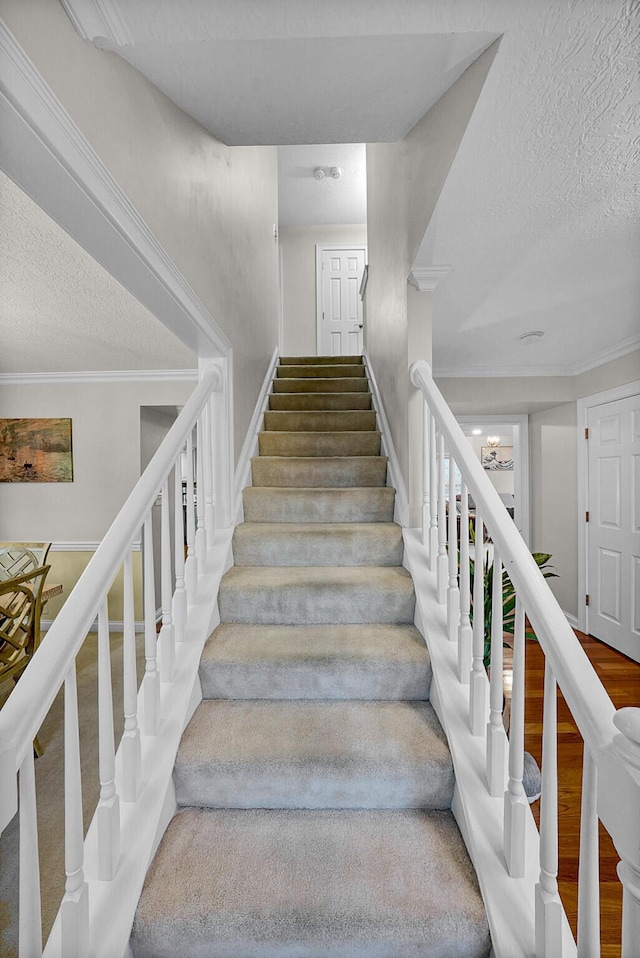 staircase with wood-type flooring, a textured ceiling, and crown molding