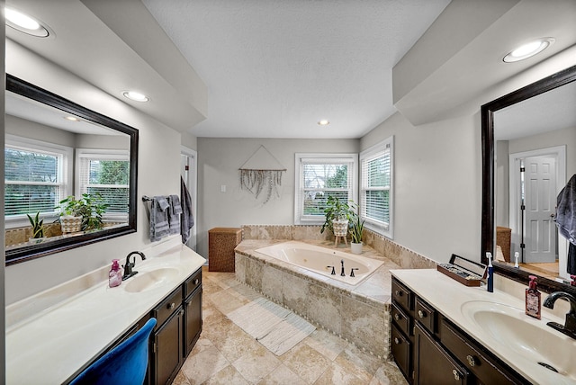 bathroom with vanity, a relaxing tiled tub, and a healthy amount of sunlight