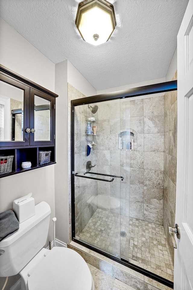 bathroom featuring toilet, a shower with shower door, and a textured ceiling