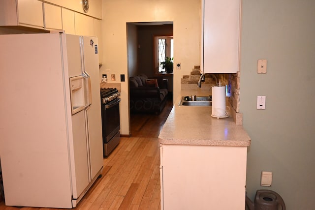 kitchen with sink, light hardwood / wood-style flooring, stainless steel range with gas cooktop, white refrigerator with ice dispenser, and white cabinets