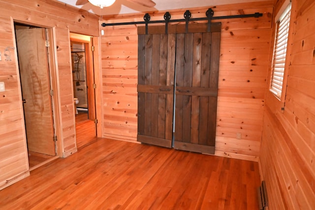 unfurnished bedroom featuring hardwood / wood-style flooring, a barn door, and wood walls