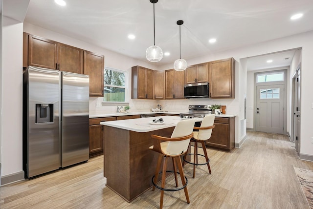 kitchen with a center island, stainless steel appliances, a kitchen breakfast bar, pendant lighting, and light wood-type flooring