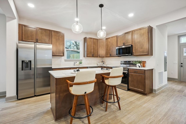 kitchen with a center island, light hardwood / wood-style flooring, appliances with stainless steel finishes, decorative light fixtures, and a kitchen bar