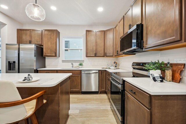 kitchen with sink, decorative light fixtures, light hardwood / wood-style floors, a kitchen bar, and stainless steel appliances