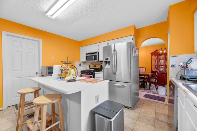 kitchen featuring backsplash, a breakfast bar area, a textured ceiling, white cabinetry, and stainless steel appliances