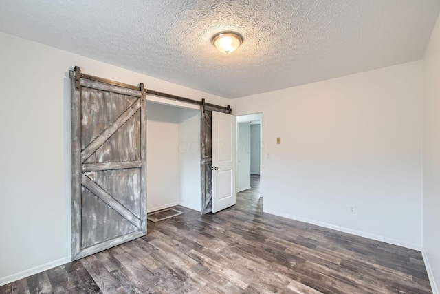 unfurnished room featuring a textured ceiling, a barn door, and dark hardwood / wood-style floors