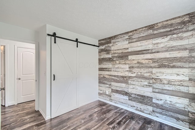 unfurnished bedroom with a textured ceiling, a barn door, dark wood-type flooring, and wooden walls