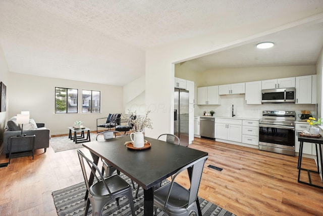 dining room with a textured ceiling, light hardwood / wood-style flooring, and lofted ceiling