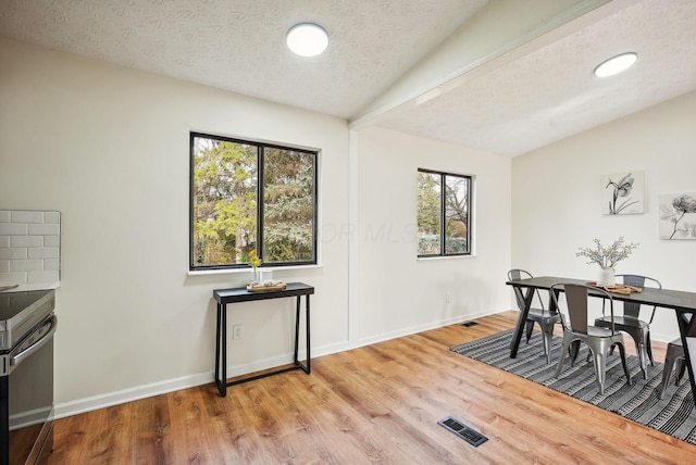 dining space with light wood-type flooring, a textured ceiling, and lofted ceiling