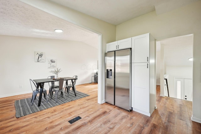 kitchen featuring stainless steel refrigerator with ice dispenser, vaulted ceiling, a textured ceiling, white cabinets, and light wood-type flooring