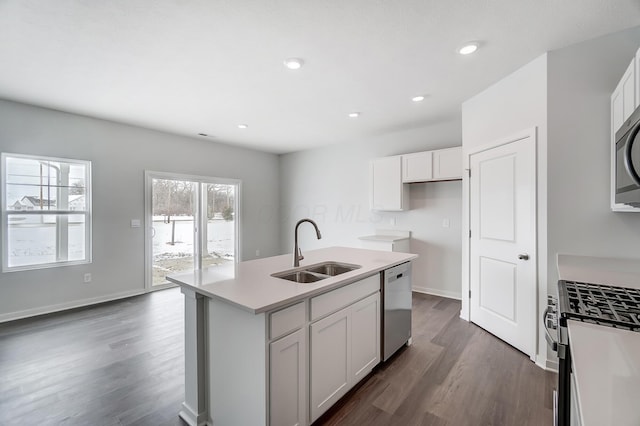 kitchen with dark wood-type flooring, a center island with sink, sink, white cabinetry, and stainless steel appliances