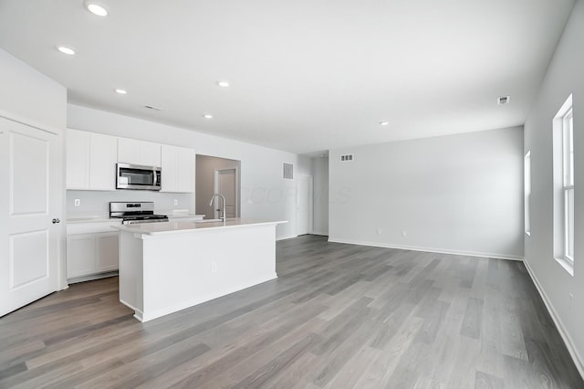 kitchen featuring appliances with stainless steel finishes, sink, light hardwood / wood-style flooring, white cabinetry, and an island with sink