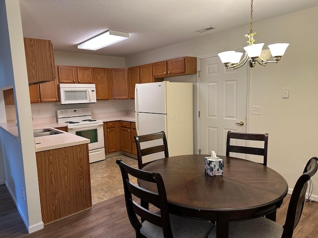 kitchen featuring white appliances, decorative light fixtures, a textured ceiling, a notable chandelier, and dark hardwood / wood-style flooring