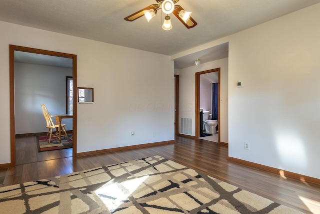 empty room with ceiling fan, dark wood-type flooring, and a textured ceiling