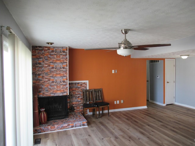 sitting room featuring a stone fireplace, ceiling fan, wood-type flooring, and a textured ceiling