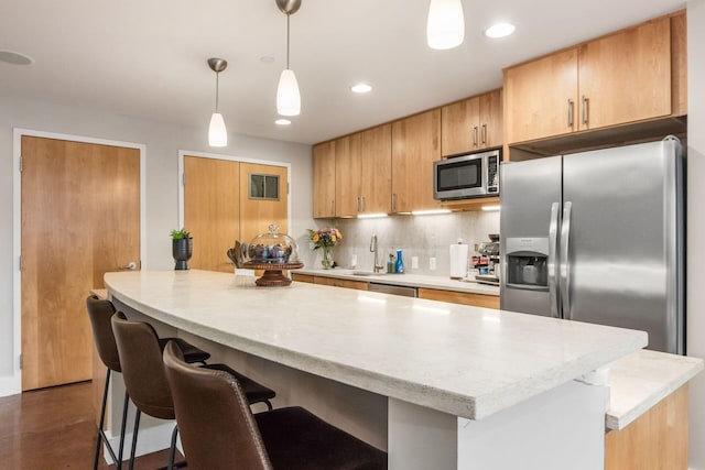 kitchen with a breakfast bar, sink, appliances with stainless steel finishes, tasteful backsplash, and decorative light fixtures