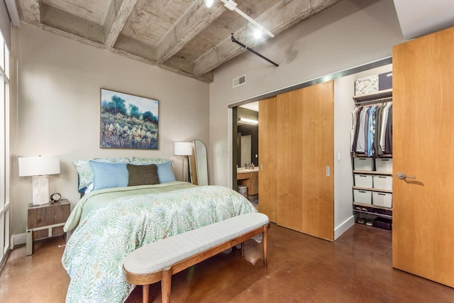 bedroom with concrete flooring, connected bathroom, and a closet