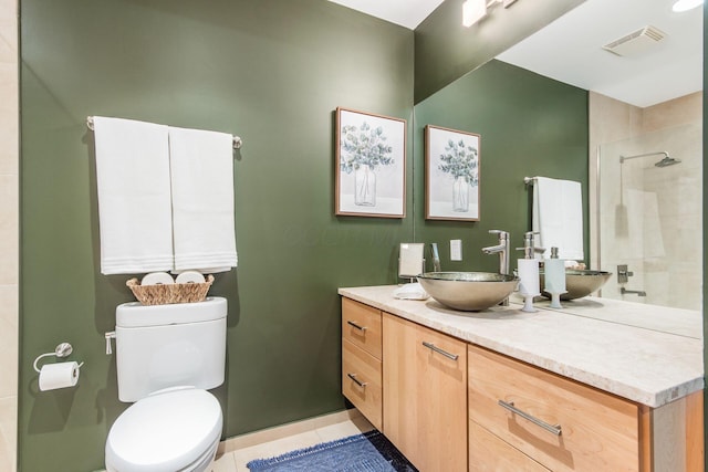 bathroom with toilet, vanity, tiled shower, and tile patterned floors