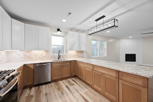 kitchen with sink, hanging light fixtures, stainless steel appliances, light hardwood / wood-style floors, and a fireplace