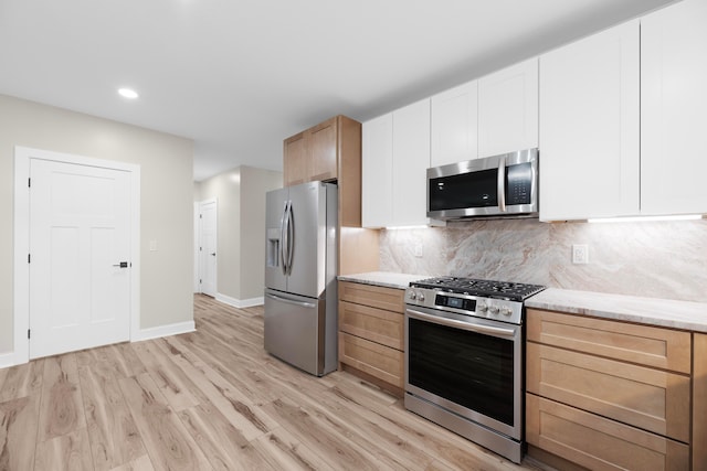 kitchen with light stone countertops, light wood-type flooring, appliances with stainless steel finishes, tasteful backsplash, and white cabinetry