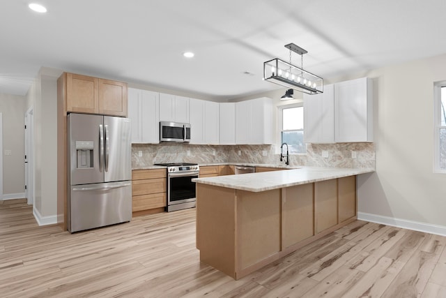 kitchen with kitchen peninsula, light wood-type flooring, stainless steel appliances, sink, and pendant lighting