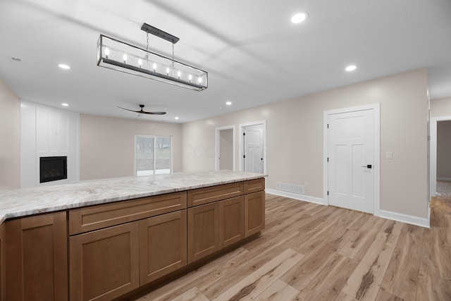 kitchen with light stone countertops, ceiling fan, hanging light fixtures, light hardwood / wood-style flooring, and a fireplace