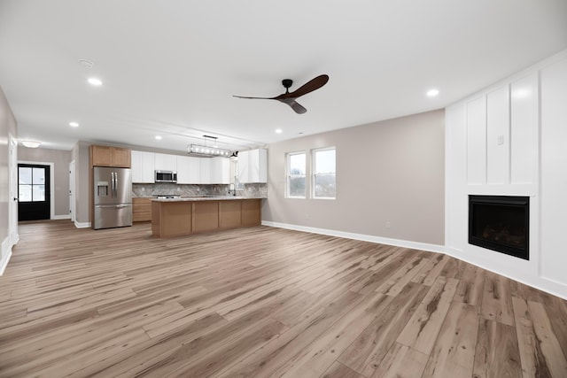 unfurnished living room featuring a large fireplace, light hardwood / wood-style floors, and ceiling fan