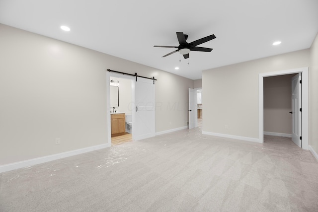 unfurnished bedroom with a barn door, ceiling fan, ensuite bath, and light carpet