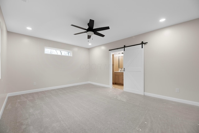 carpeted spare room featuring a barn door and ceiling fan