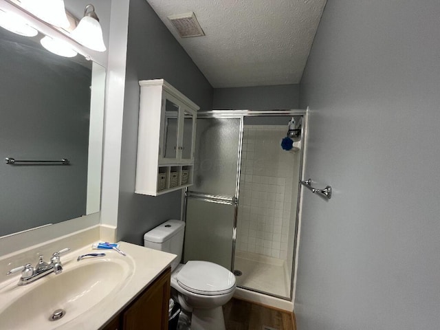 bathroom featuring vanity, toilet, a shower with shower door, and a textured ceiling