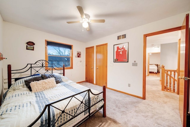 bedroom featuring two closets, light colored carpet, and ceiling fan