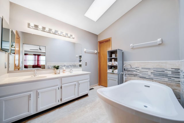 bathroom featuring vaulted ceiling with skylight, tile patterned flooring, vanity, ceiling fan, and a bath