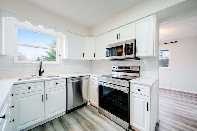 kitchen with stainless steel appliances, white cabinetry, light hardwood / wood-style floors, and sink