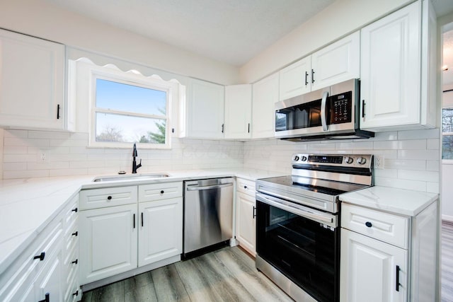 kitchen featuring white cabinets, sink, light wood-type flooring, appliances with stainless steel finishes, and tasteful backsplash