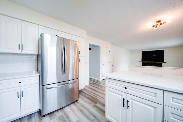 kitchen featuring decorative backsplash, light stone countertops, light wood-type flooring, white cabinets, and stainless steel refrigerator