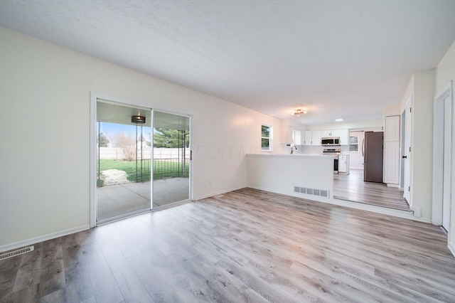 unfurnished living room featuring a textured ceiling, light hardwood / wood-style floors, and sink