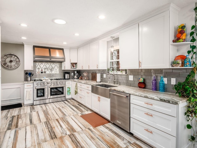 kitchen with white cabinets, sink, wall chimney range hood, and stainless steel appliances