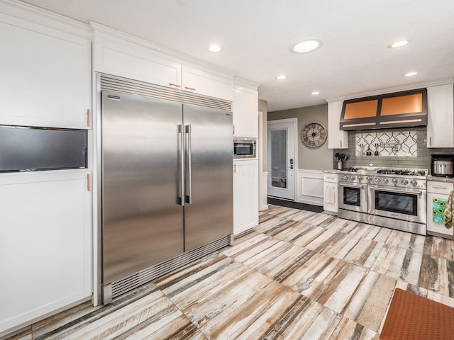 kitchen with built in appliances, premium range hood, white cabinetry, and backsplash