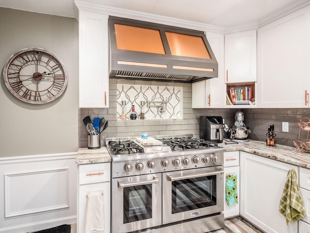 kitchen with white cabinets, range with two ovens, wall chimney range hood, and light stone counters