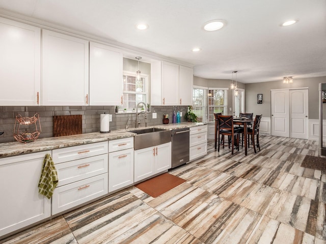 kitchen with light stone countertops, white cabinetry, sink, hanging light fixtures, and decorative backsplash