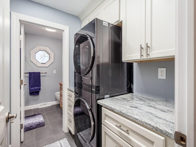 washroom featuring cabinets, stacked washing maching and dryer, and dark tile patterned floors