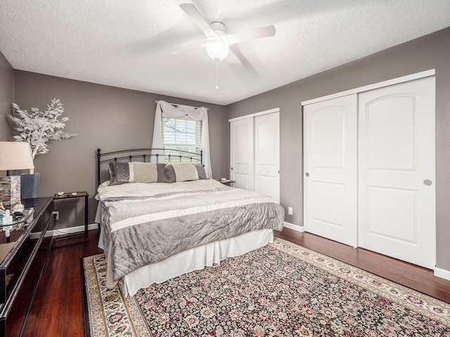 bedroom featuring dark hardwood / wood-style floors, ceiling fan, a textured ceiling, and two closets