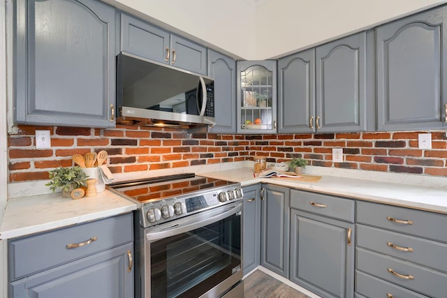 kitchen featuring appliances with stainless steel finishes, dark hardwood / wood-style flooring, gray cabinets, and backsplash