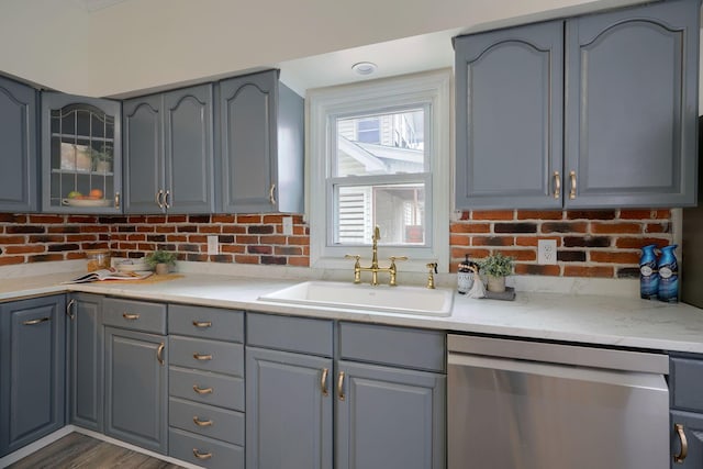 kitchen with light stone counters, stainless steel dishwasher, gray cabinetry, dark wood-type flooring, and sink