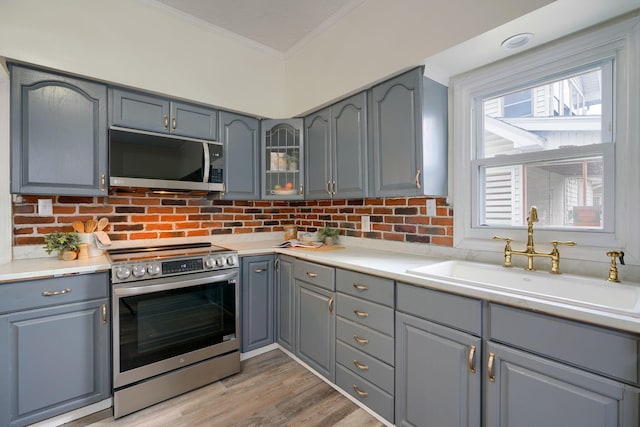 kitchen with backsplash, stainless steel appliances, crown molding, sink, and light hardwood / wood-style floors