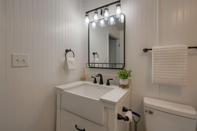 bathroom featuring vanity, toilet, and wooden walls